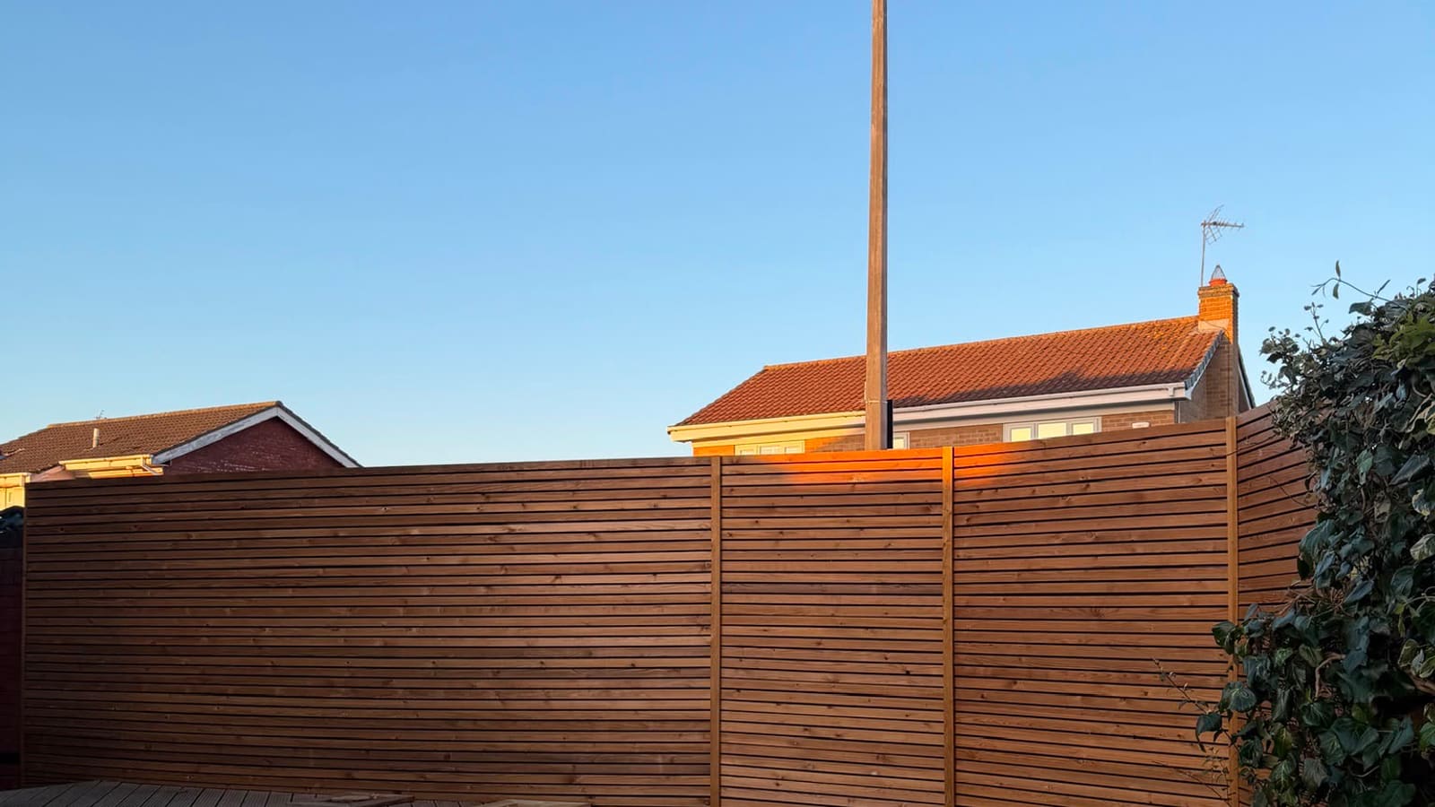 Contemporary slatted fence and new decking by Maxwell Property Services, lit by evening sun