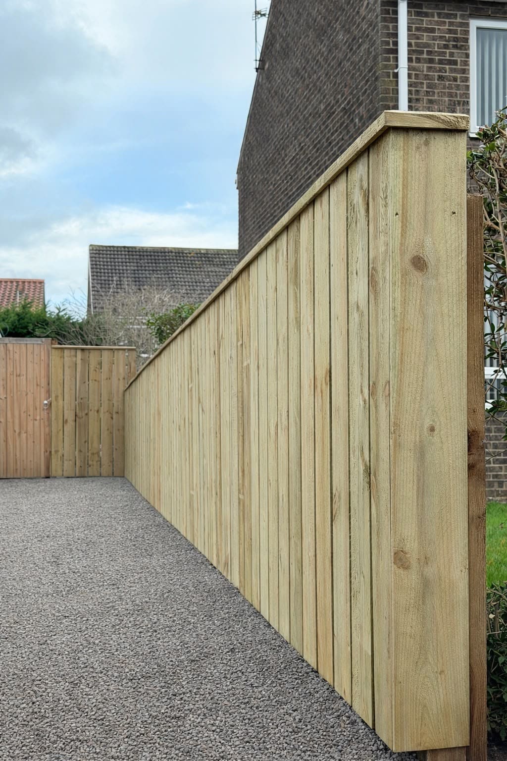 New tanalised closeboard fence with capping rail stepping down alongside a gravel driveway